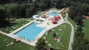 A large swimming pool surrounded by sun loungers and umbrellas, with a water slide and a building in the background.