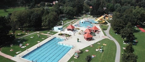 Une grande piscine entourée de chaises longues et de parasols, avec un toboggan aquatique et un bâtiment en arrière-plan.