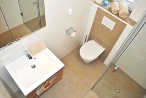 Un baño moderno con lavamanos, inodoro y zona de ducha blancos.
