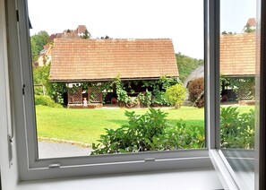 A view through a window of a building with a brick facade, a covered porch, and a well-maintained lawn.