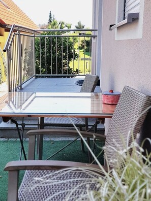 Un balcón con una mesa y sillas, barandilla y vistas a un jardín y un edificio.