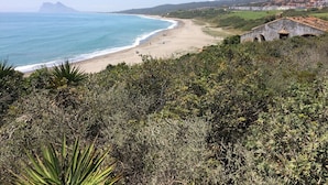 Un paisaje costero con una playa, una colina con vegetación y un edificio de techo de piedra.
