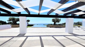 Un área de patio techada al aire libre con vista al mar, paredes de piedra y una piscina.