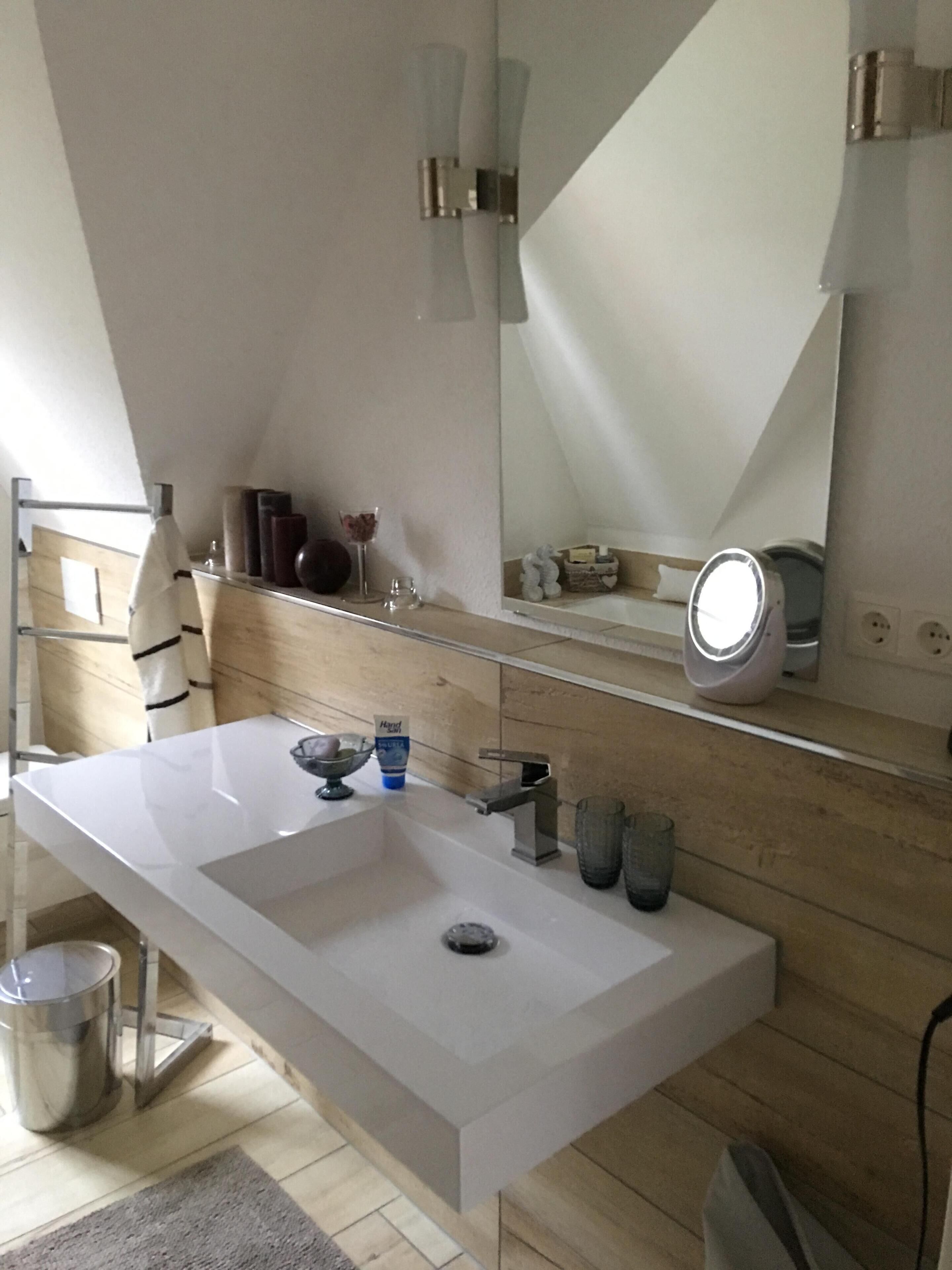 Ein modernes Badezimmer mit einem weißen Waschbecken, einem Spiegel und einem Handtuchhalter.