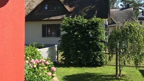 Una casa tradicional con techo de paja, un césped bien cuidado y un jardín con flores rosadas.