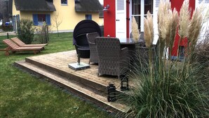 Un patio con mobiliario exterior, una parrilla y plantas decorativas.