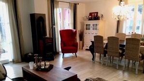 Un salón con chimenea, un sillón rojo, una mesa de comedor con sillas de mimbre y una araña.