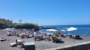 A beach with lounge chairs and umbrellas, rocky shoreline, and clear blue sky. - Apartment with sun terrace and panoramic sea view, 5 min. from harbor + beach (Los Gigantes)