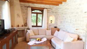 Una sala de estar acogedora con una pared de piedra, un sofá beige, una mesa de centro de madera con fruta y un televisor sobre un mueble de madera.