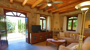 Una sala de estar acogedora con chimenea de piedra, vigas de madera en el techo, un televisor y un sofá.