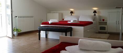 A modern hotel room with a bed, a bench, a red rug, and a white bench with towels.