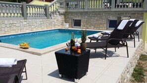 A poolside area with lounge chairs, a table with fruits and drinks, and a stone wall. - Beautiful villa / app **** with swimming pool, 900 m from the sea, WiFi, barbecue (Vintijan)