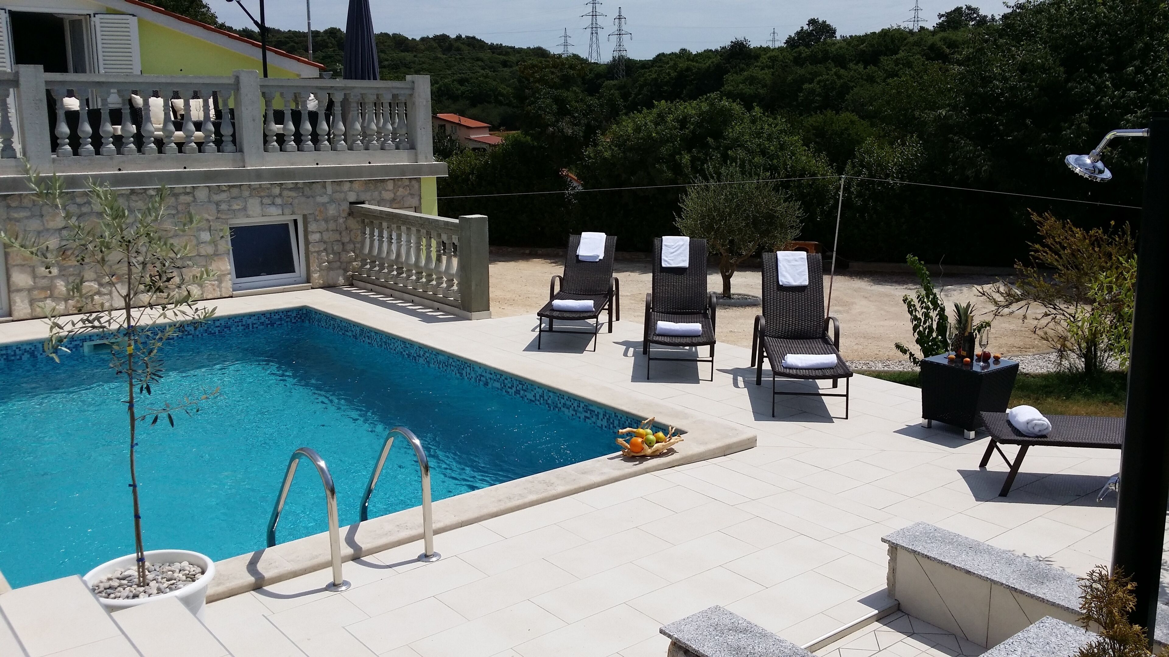 Zona de piscina con pared de piedra, sillones de descanso y una mesa con frutas.
