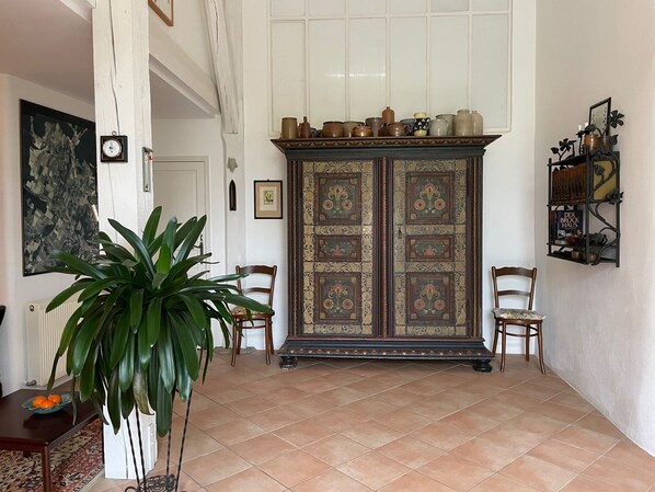 A room with a large cabinet, two chairs, a potted plant, and a tiled floor.