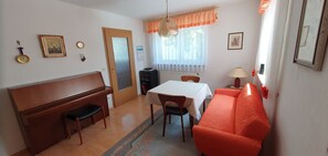 Een kamer met een piano, een eettafel, een bank en een radiator.