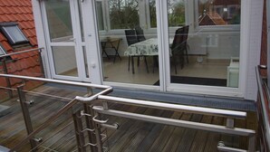 Ein überdachter Patio-Bereich mit Tisch und Stühlen, einem Fenster und Blick auf die Umgebung.
