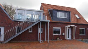 Ein zweistöckiges Ziegelhaus mit rotem Ziegeldach, einem Balkon und einer Treppe, die zum Obergeschoss führt.