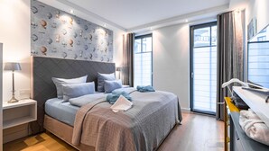 A modern bedroom with a large bed, a headboard with a geometric pattern, a wall with a shell print, and a window with curtains. - Luxury Seebrise Binz: Fireplace, Park Setting, and Perfect for a Vacation with Your Dog (Binz)