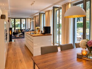 A modern kitchen with a central island, a dining area with a wooden table, and a living room with a sofa and coffee table.