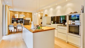 A modern kitchen with a central island, built-in appliances, and a dining area with chairs and a table. - Luxury Seebrise Binz: Fireplace, Park Setting, and Perfect for a Vacation with Your Dog (Binz)
