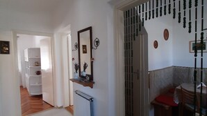 A hallway with a radiator, a mirror, and a hanging light fixture. There is a door leading to a room with a chair and a table.