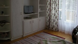 A room with a TV on a shelf, a floral curtain, and a patterned rug.