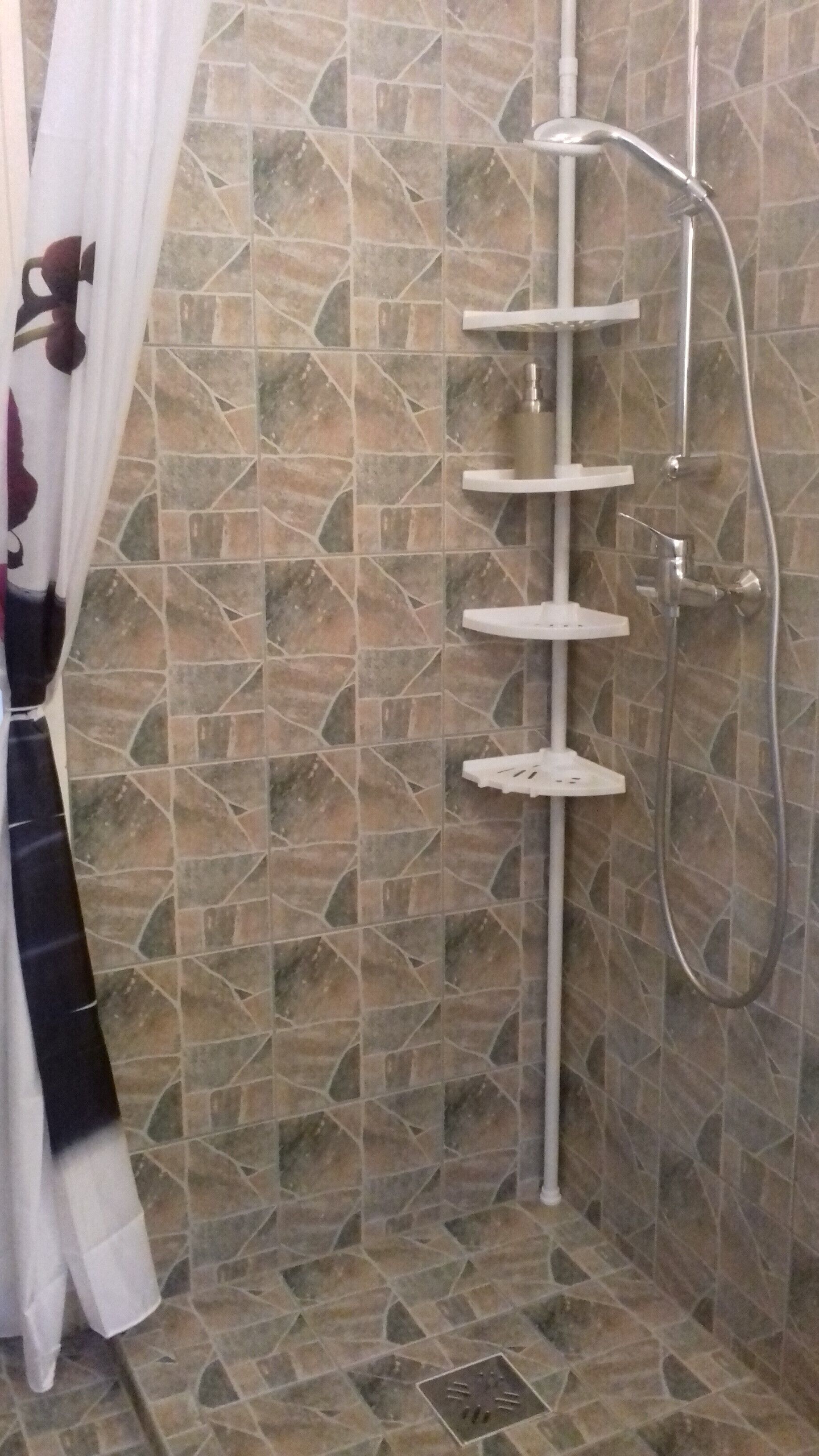 Eine Dusche mit einer bodenständigen Regendusche und einer Handbrause, vor einer Wand mit geometrischem Fliesendesign.