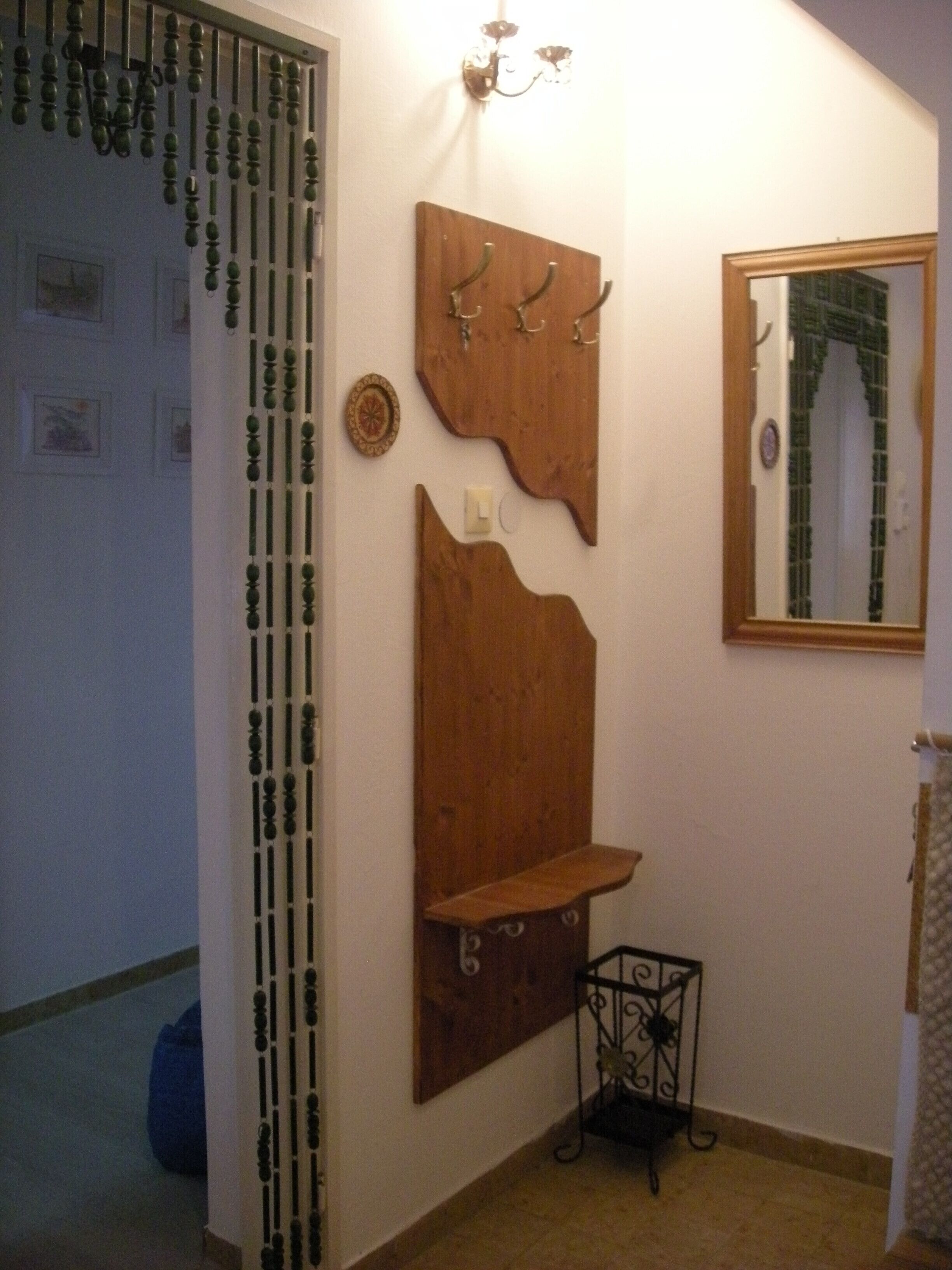 A bathroom with a wooden wall-mounted shelf, a mirror, and a decorative light fixture.