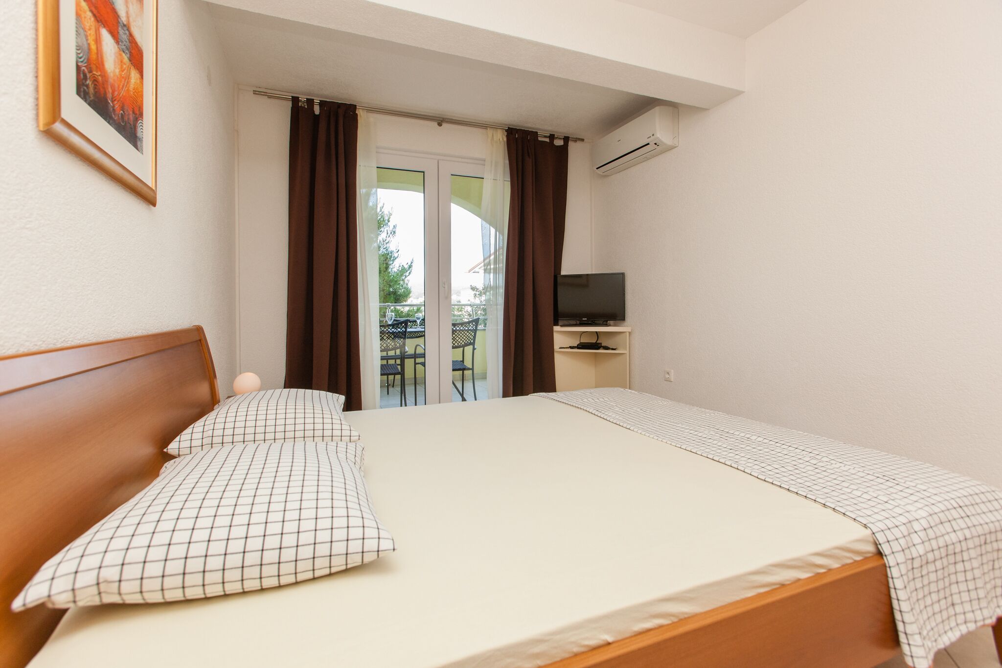 A hotel room with a bed, a TV, and a balcony with a table and chairs.