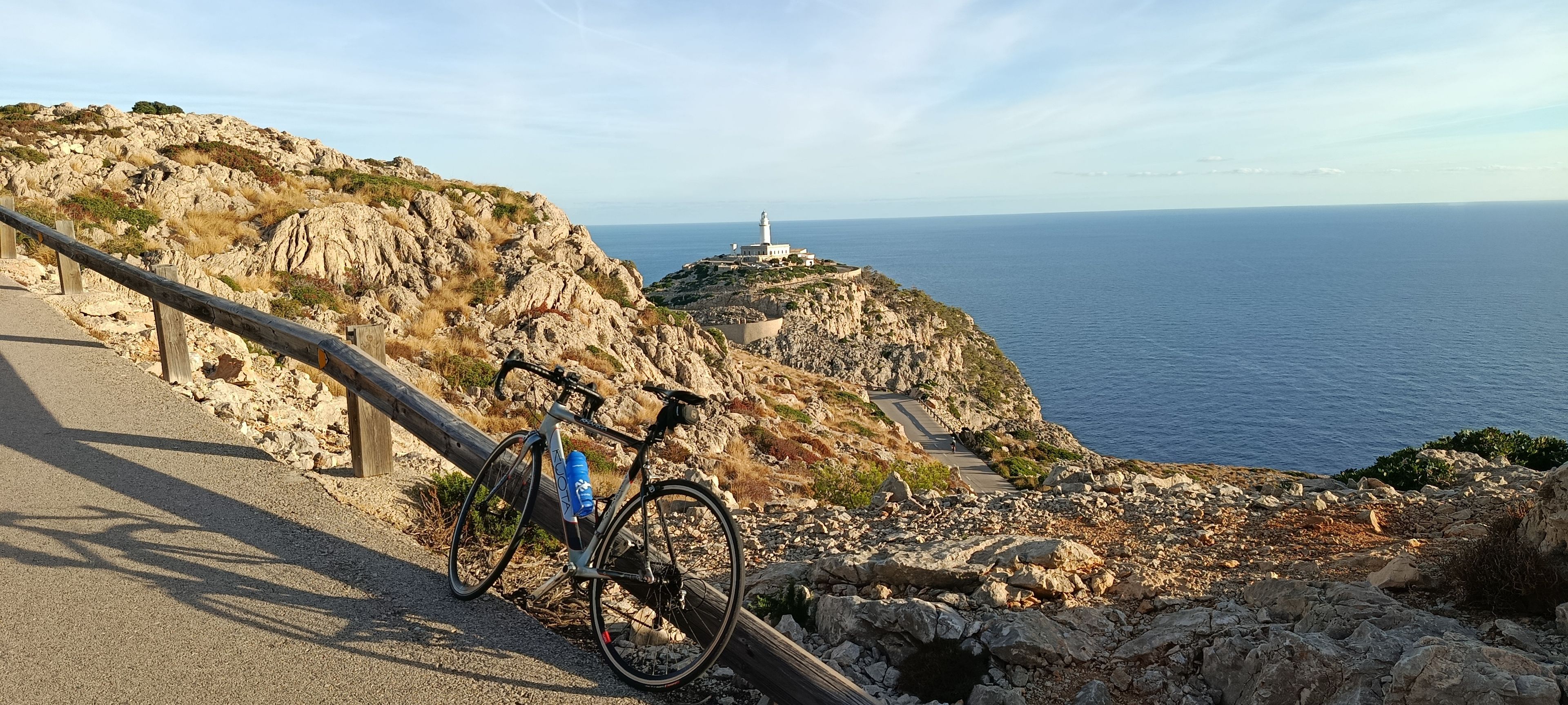 A bicycle parked on a rocky coastal road with a lighthouse in the background.