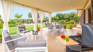 A covered patio with outdoor furniture, a grill, and potted plants.