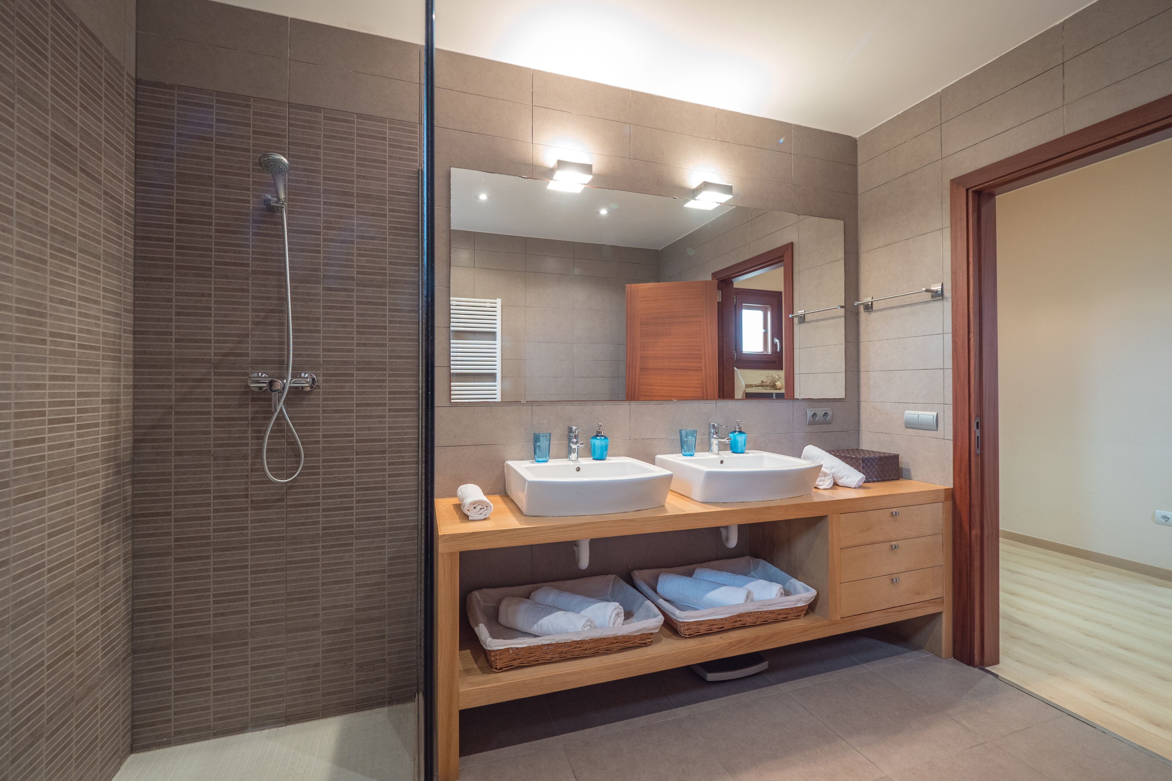 Een moderne badkamer met twee wasbakken, een douche en een spiegel.