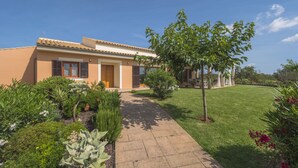 A modern house with a paved driveway leading to the entrance, surrounded by well-maintained gardens and a clear blue sky.