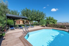 A swimming pool with a wooden deck, lounge chairs, and a covered seating area.