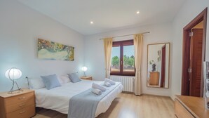 A bedroom with a large bed, bedside tables, a painting, a window with curtains, a mirror, and a wooden dresser.