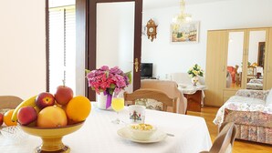 Un comedor con una mesa preparada para dos personas, con un frutero, un vaso de jugo y un plato con un cuenco pequeño de nueces.