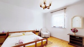 A bedroom with a wooden bed, a chair, a bedside table, a mirror, and a window with curtains.