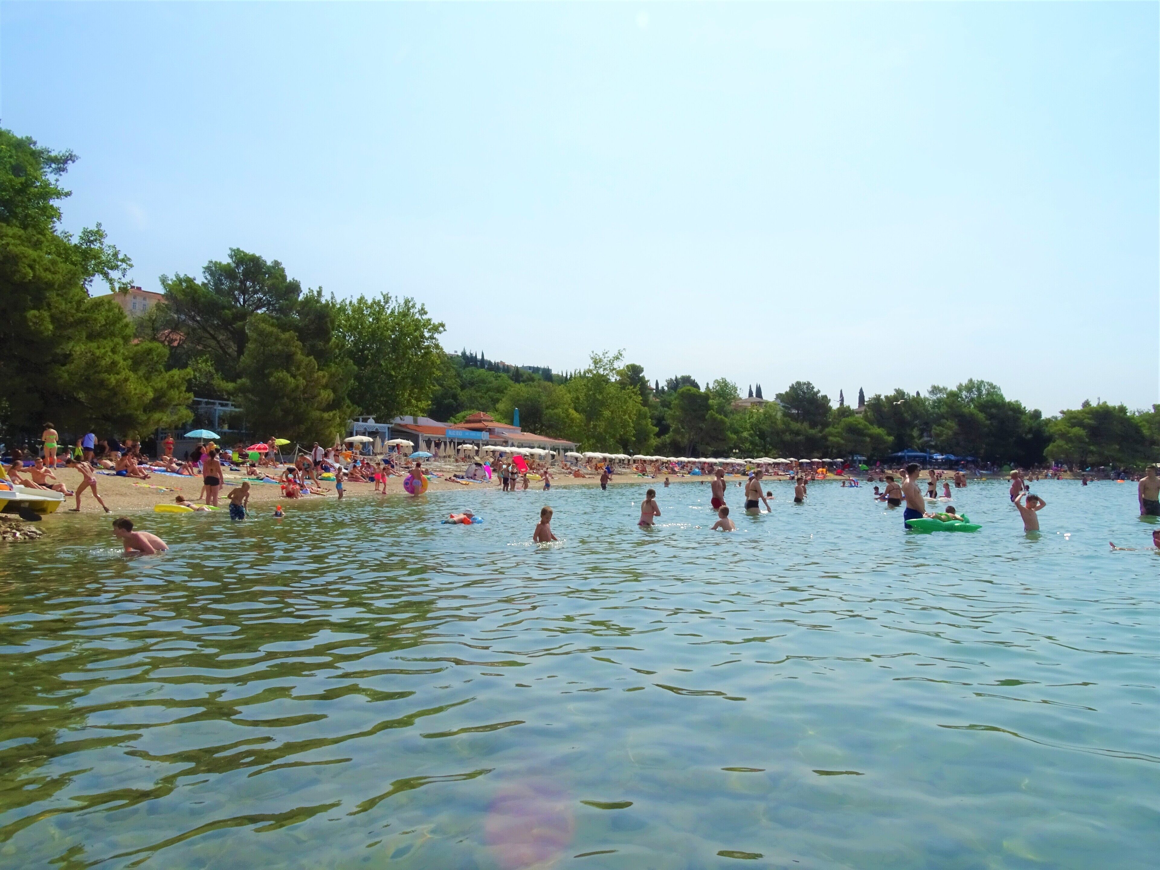 A crowded beach with people swimming and sunbathing.