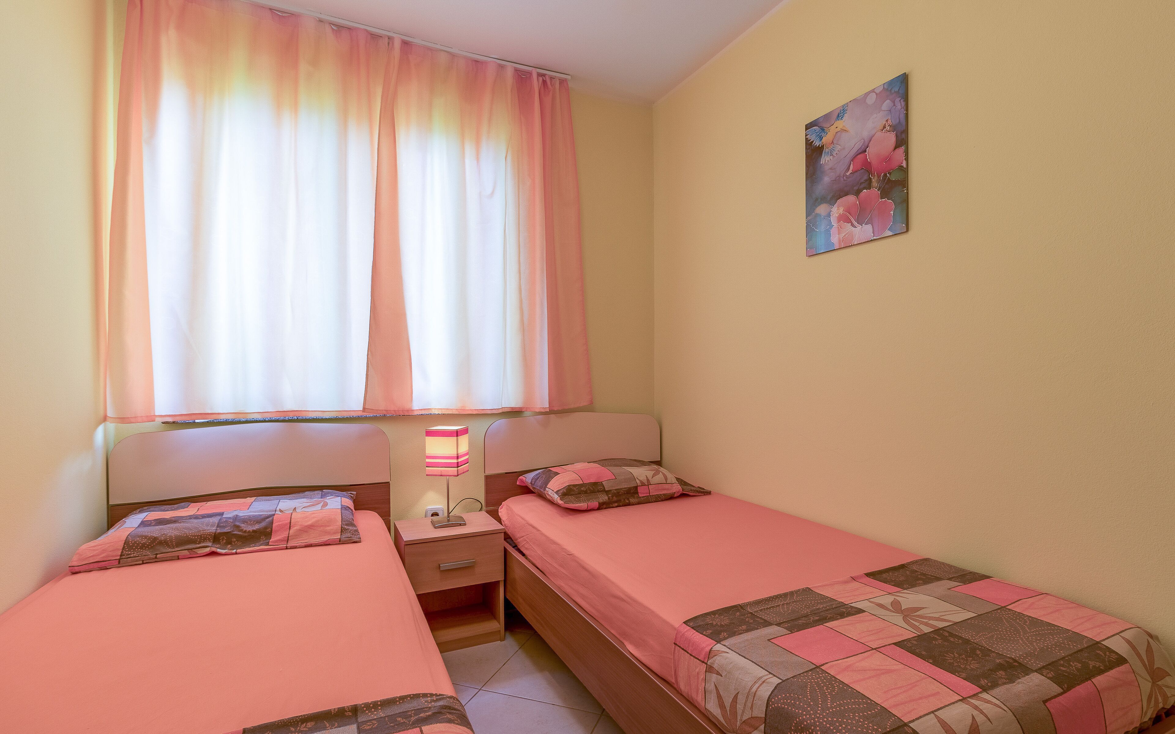 A bedroom with two single beds, a nightstand, a lamp, and a painting on the wall.