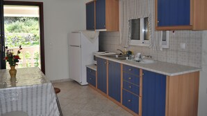 A compact kitchen with blue cabinets, a white refrigerator, and a window with curtains. - Beach house Tolis at Pelekas Beach (Pelekas Κέρκυρα)