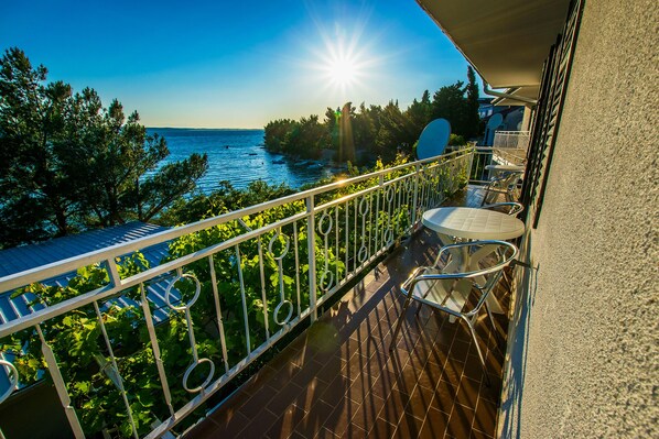 A balcony with a view of the sea, a table, and chairs.