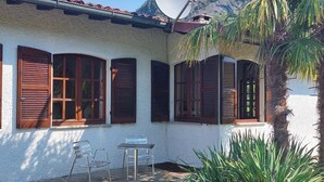 A house with a satellite dish, a patio with a table and chairs, and a palm tree. - Spacious vacation home with garden, approx. 150 m to the lake, with bathing facilities (Lavena Ponte Tresa)