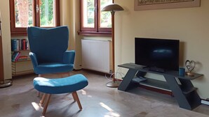A living room with a blue armchair, a television, and a bookshelf. - Spacious vacation home with garden, approx. 150 m to the lake, with bathing facilities (Lavena Ponte Tresa)