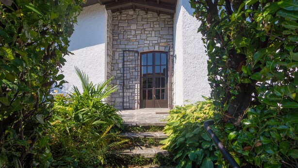 A stone building with a wooden door and steps leading up to it, surrounded by lush greenery. - Spacious vacation home with garden, approx. 150 m to the lake, with bathing facilities (Lavena Ponte Tresa)
