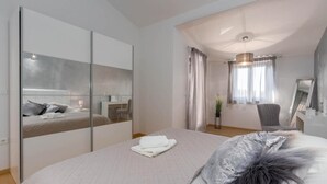 A modern bedroom with a large bed, a desk, and a mirror.
