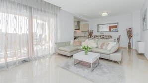A modern living room with a sectional sofa, a coffee table, and a large window with sheer curtains.