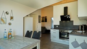 A modern kitchen with white cabinets, a stainless steel oven, and a dining area with a wooden table and chairs. - Vacation magic  (Neukirch)