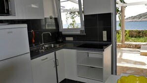 Cocina compacta con armarios blancos, encimera negra y vista al mar.