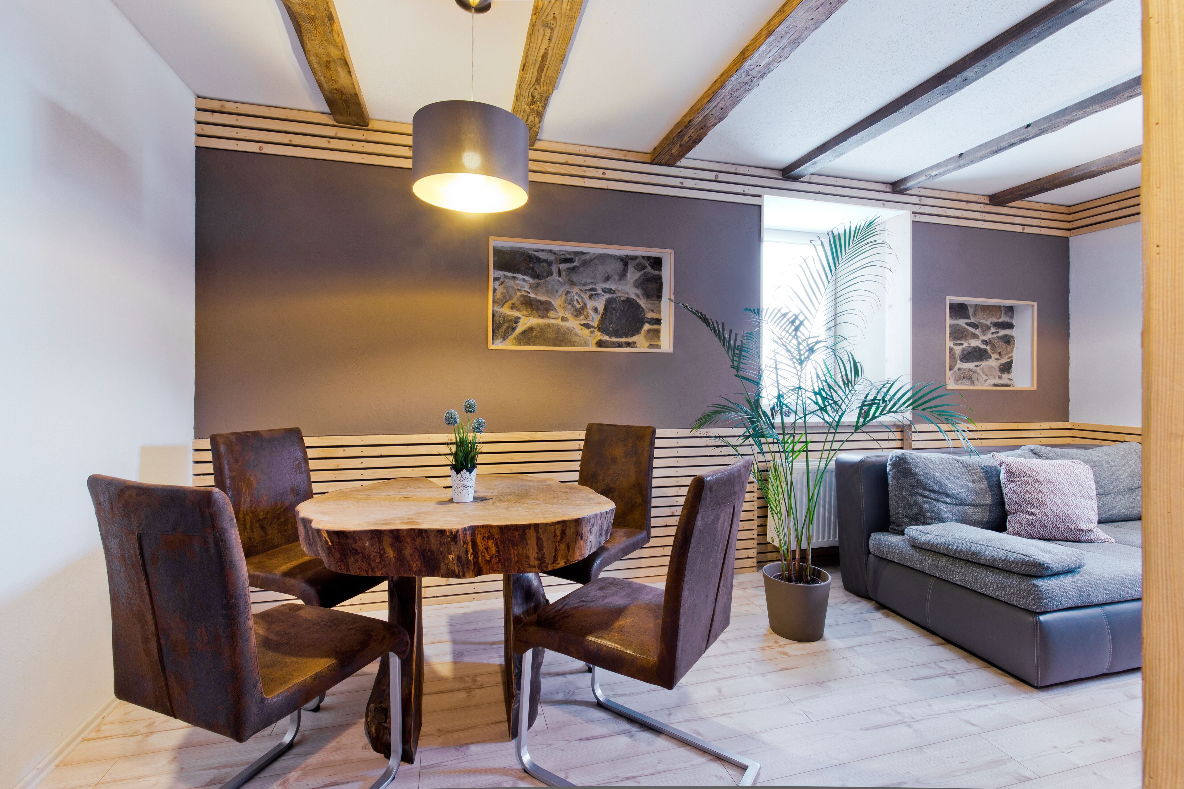 A modern living room with a round wooden table, metal chairs, a grey sofa, and a potted plant.