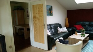 A living room with a black leather sofa, a wooden door, a small table with bottles, and a painting on the wall. - Holiday house in the Lüneburg Heath up to 4 people (Suderburg)